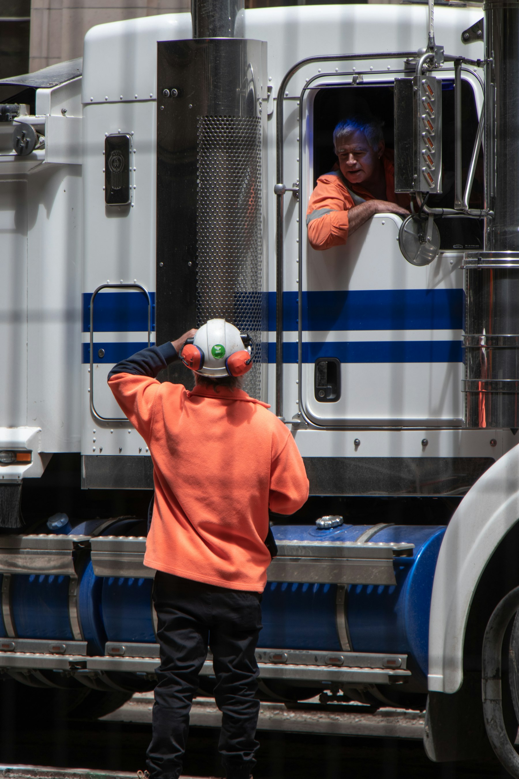 Driver in a hard hat and orange jacket beside a semi truck cab