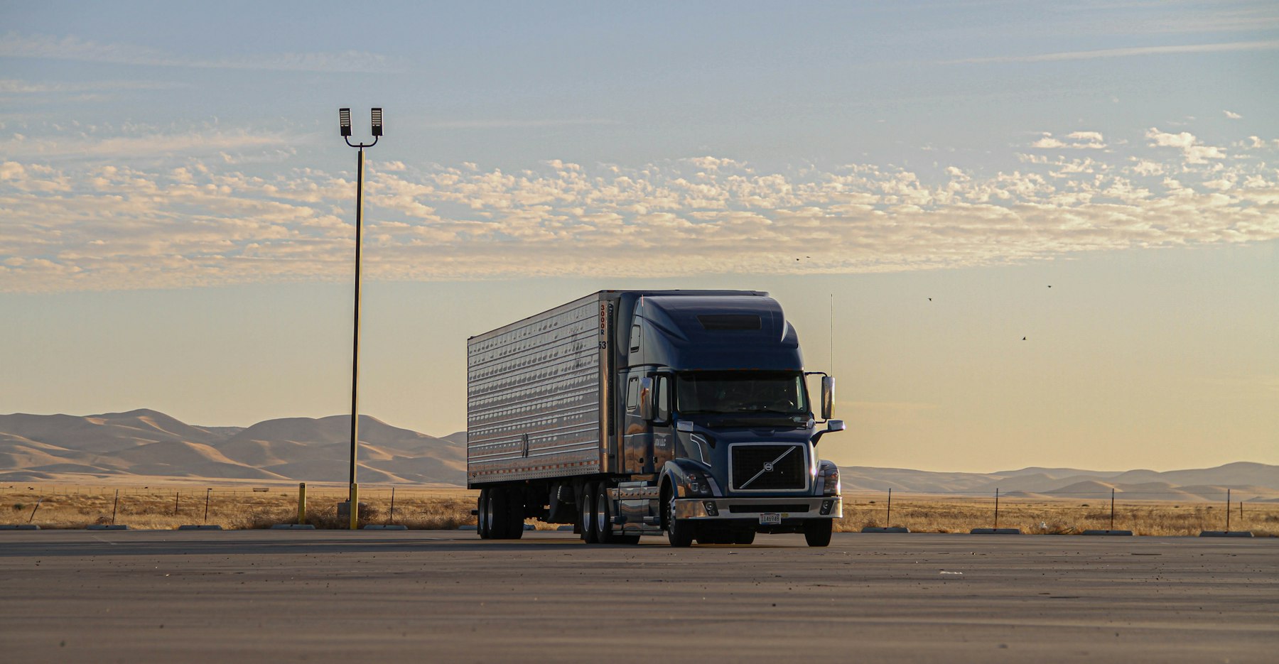 Dark semi truck pulling a dry van trailer on an open road