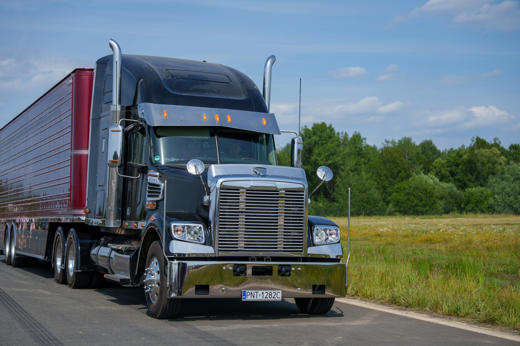Black semi truck driving a rural road with trees along the shoulder