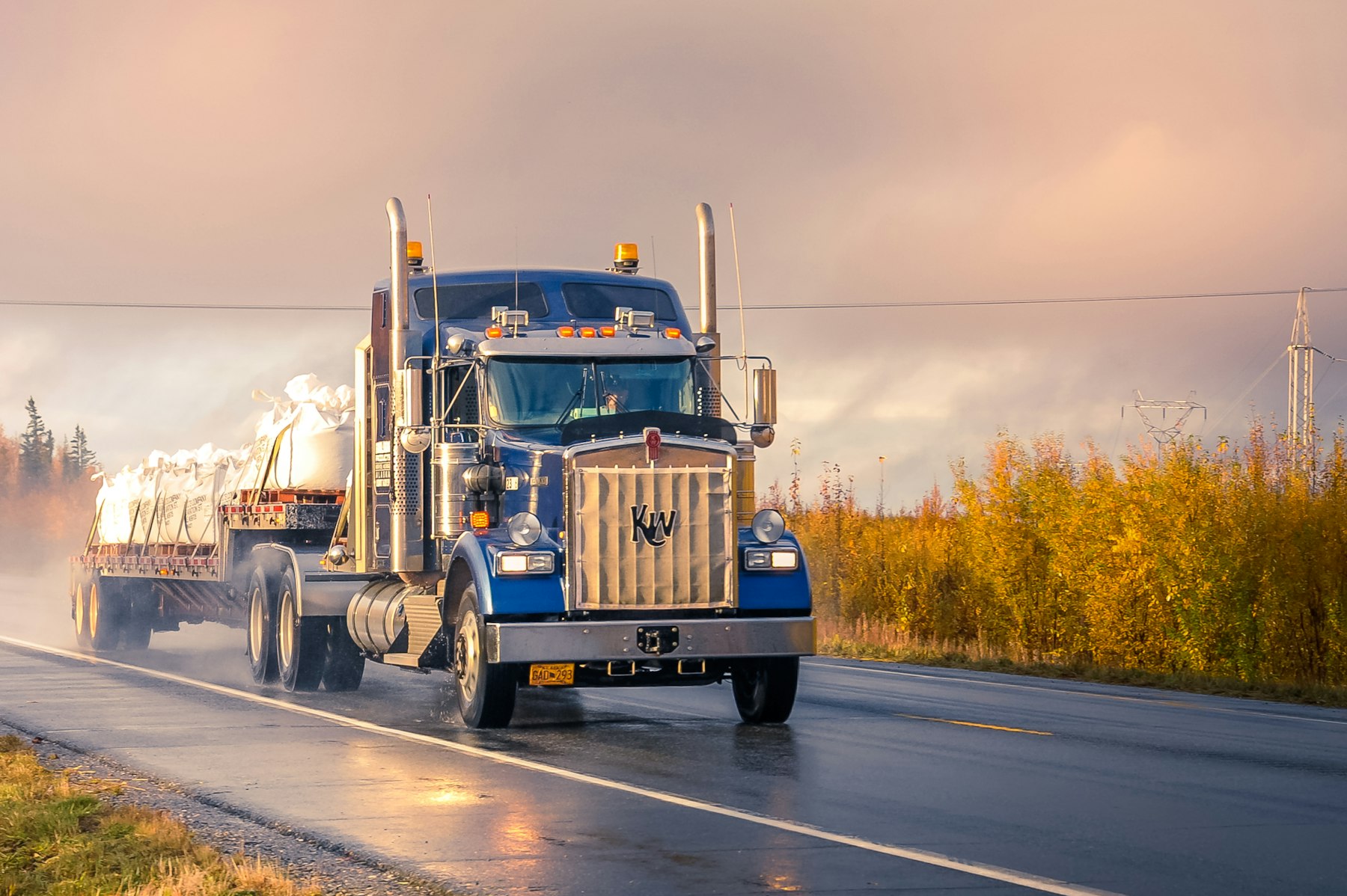 Blue conventional semi truck hauling a load on a rural American road