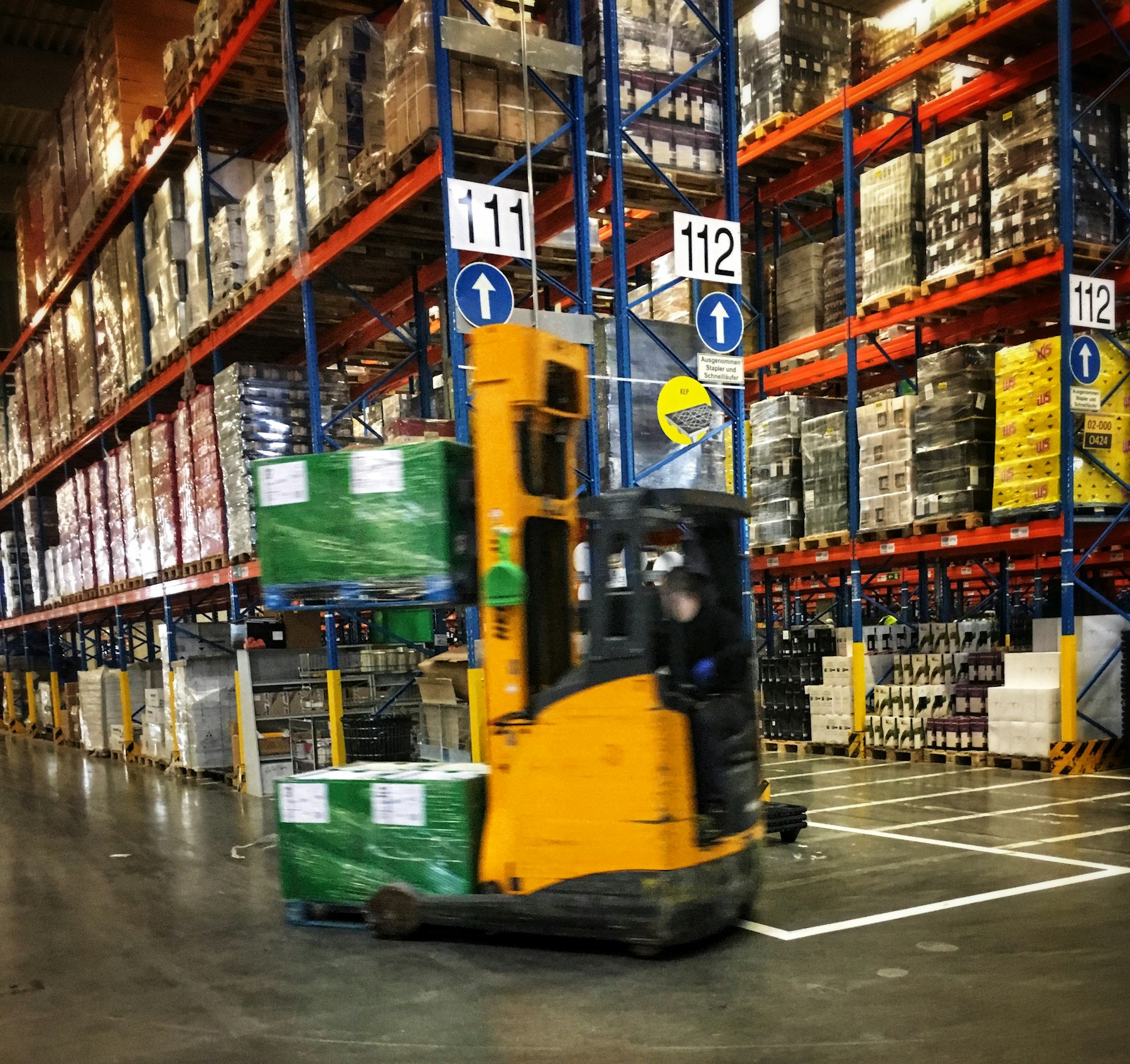 Reach truck moving pallets through a racked warehouse aisle